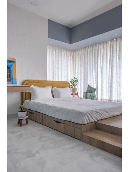 Inviting a rustic vibe, this daughter's room features a brick wall, a playful C-shaped wooden platform bed, and a mustard headboard, adding vibrant color and personality to the space.