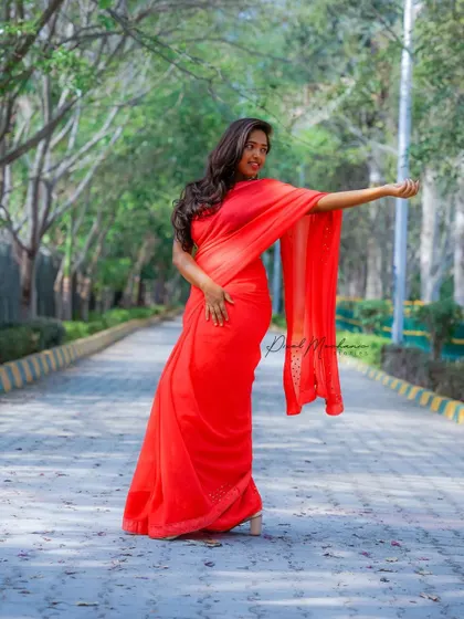 The striking red saree against the tree-lined avenue creates a powerful and cinematic image. This is a great example of an outdoor ethnic wear portrait.
