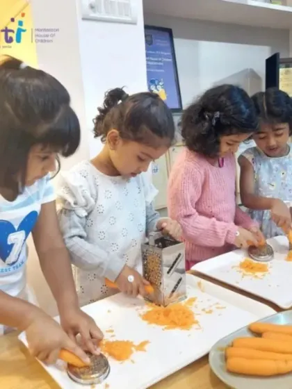 With great focus, a group of girls grate carrots for their tricolour salad. Using real kitchen tools under supervision builds their confidence and practical abilities.
