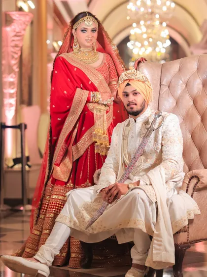 A regal portrait of a Sikh bride and groom. The groom is seated while the bride stands beside him, creating a powerful and traditional composition.
