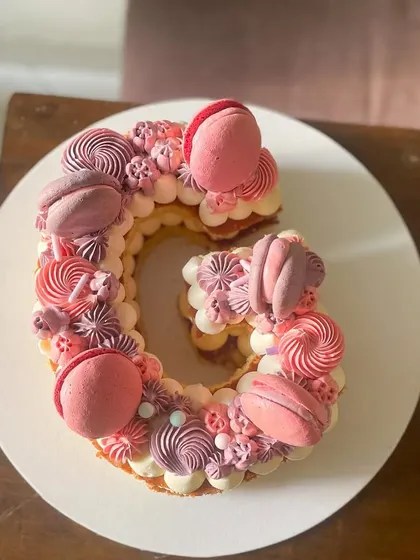 Letter cakes are a fun and personal way to celebrate. This 'G' monogram cake is decorated with beautiful monochrome buttercream swirls in shades of pink and purple, topped with matching macarons.