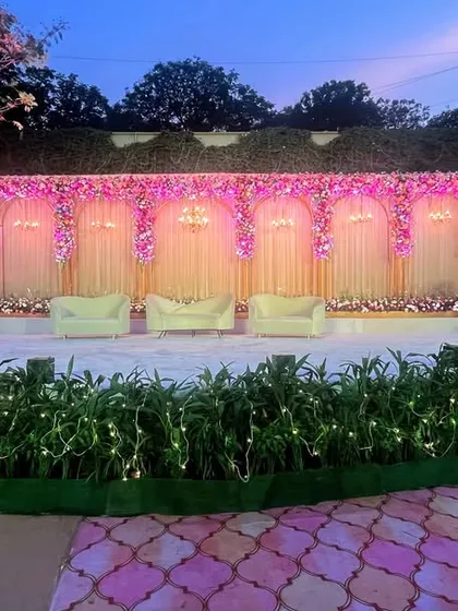 As dusk settles, this outdoor reception stage comes to life with beautiful pink lighting. The floral arrangements across the top and the fairy lights in the foreground create a warm and inviting atmosphere.