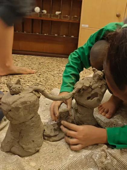 A child's hands are deep in the creative process, shaping the natural clay into a family of animal figures.