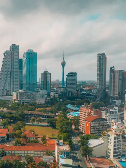 An aerial view of the Colombo skyline, featuring the distinctive Lotus Tower. This perspective shows the mix of modern skyscrapers and lush green spaces in the city.