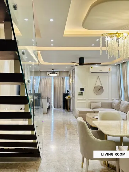 This open-plan living and dining area showcases a cohesive design with neutral tones, a stunning crystal chandelier, and a glass-paneled staircase that adds to the sense of space.