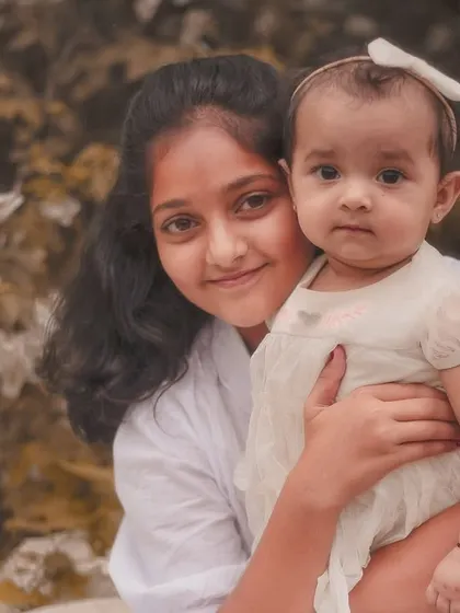 A simple, beautiful portrait of an older sister holding her baby sibling. The natural outdoor background and soft lighting create a timeless feel.