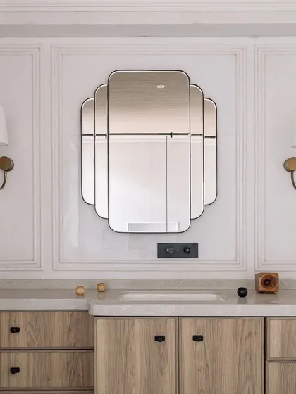The vanity area in the den's bathroom features a beautiful art-deco inspired mirror and custom wooden cabinetry. The design is clean, elegant, and timeless.