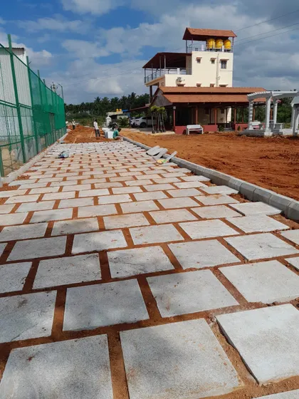 A pathway under construction, with large rectangular paving stones being laid on a prepared base of red earth. This image shows the foundational work involved in hardscaping.