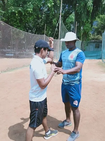 Correcting the elbow position of a young bowler. A straight arm at the point of delivery is vital for legal and effective bowling.