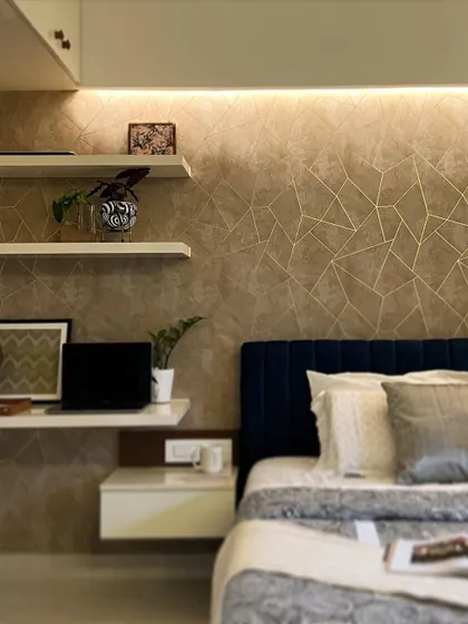 This cozy bedroom corner features a unique textured wallpaper with gold geometric lines, paired with a floating desk and shelves for a functional workspace.
