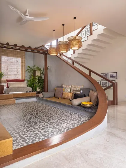 This sunken lounge area, defined by a gracefully curved wooden bench and traditional patterned tiles, creates an intimate space for conversation and connection within an open-plan layout. It’s a modern take on the traditional Indian 'baithak' or seating area.