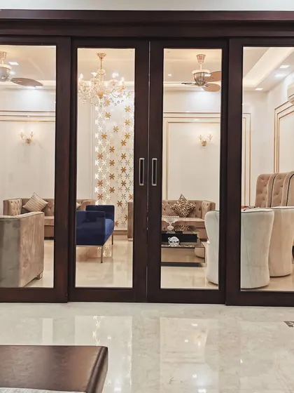 A framed view from the hallway into the formal living room of Villa 9/21B. The large, dark-stained wooden sliding doors create a dramatic threshold, separating formal and informal zones while maintaining a sense of visual connection.