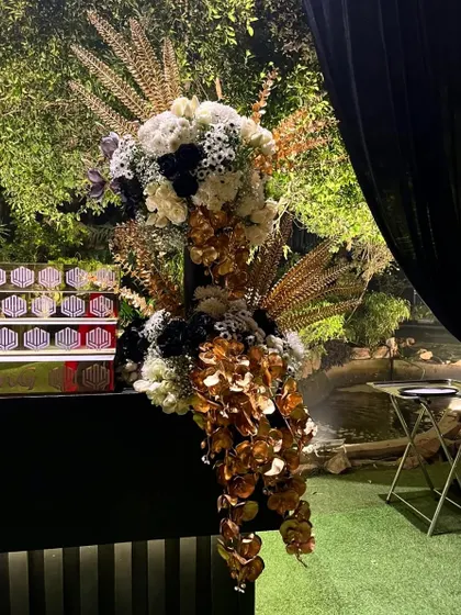 A dramatic floral cascade adorns the corner of the bar. This arrangement features white hydrangeas, black roses, and gilded phalaenopsis orchids, adding a touch of wild opulence to the structured space.