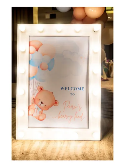 A 'Welcome to Pari's Bear-y Land' sign, framed with marquee lights, creates a warm and inviting entrance for a teddy bear-themed party.