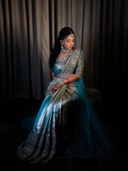 A dramatic portrait of the bride in her saree gown. The dark background highlights the shimmering fabric and intricate silver embroidery.