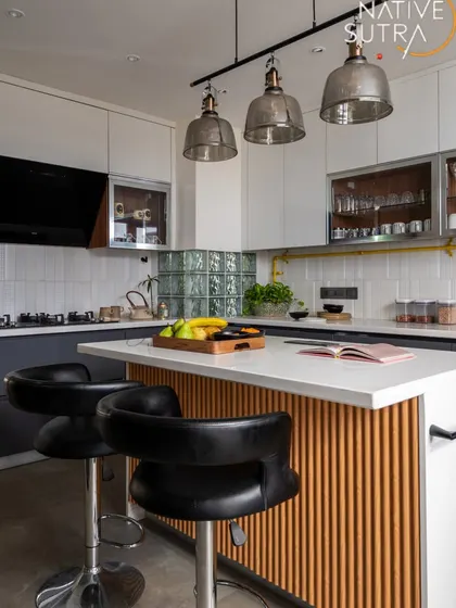 A stylish and functional kitchen with transitional charm and industrial flair. The island with a fluted wood base and comfortable bar stools serves as a casual dining spot, illuminated by glass pendant lights.