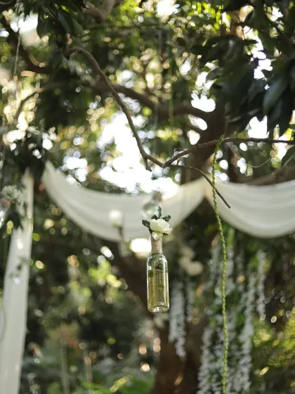 A whimsical detail of a small flower arrangement in a glass bottle hanging from a tree branch.