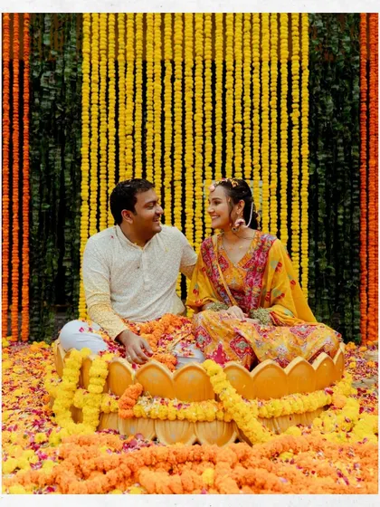 The couple sits in a lotus-shaped vessel surrounded by a sea of marigolds during their Haldi ceremony. This photo highlights the beautiful decor and happy moments of the ritual.