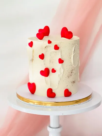A simple and sweet cake for Valentine's Day or an anniversary. The rustic white buttercream is adorned with a scattering of bright red hearts.