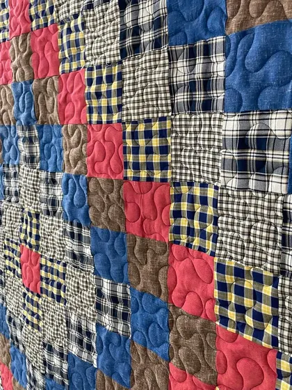 A close-up of a memory quilt made from various plaid and checked shirts, showing the cozy texture.