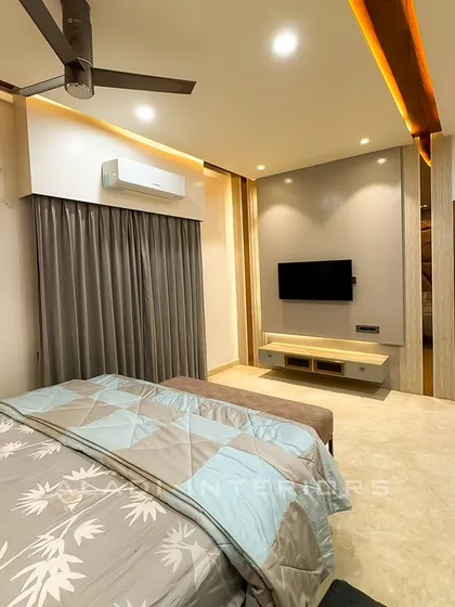 A bedroom featuring a sophisticated grey and wood theme. The TV wall is simple and elegant, and the room opens up to a dressing area.