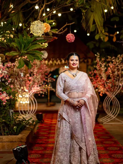 A beautiful solo portrait of the bride at her reception, glowing in her elegant pastel lehenga against a backdrop of fairy lights and flowers.