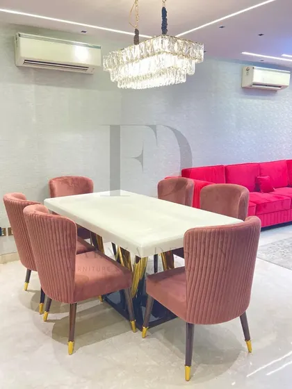 This dining set makes a bold statement with a vibrant pink velvet sofa on one side. The dusty rose chairs and white onyx table are set off by a stunning crystal chandelier, creating a glamorous look.