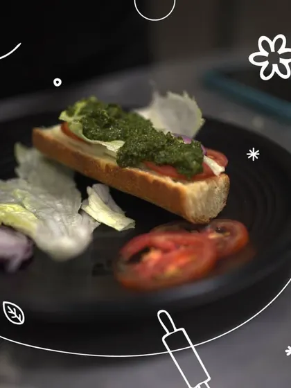 The simple pleasure of a well-made sandwich on bread you baked yourself. Here, a slice of fresh bread is topped with pesto and tomatoes, a perfect way to enjoy your creation.