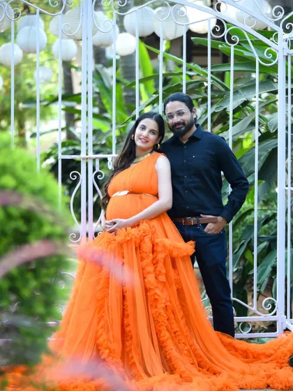 A stylish couple posing in front of an elegant white gate during their outdoor maternity session.