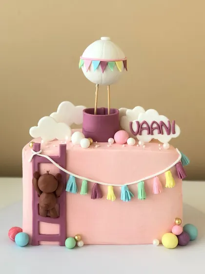A whimsical half-birthday cake with a hot air balloon and a little bear climbing a ladder.