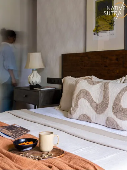 This rustic modern bedroom is infused with a touch of bohemian soul. The motion blur of a person adds a sense of life to the space, which features a dark wood headboard, textured wallpaper, and cozy, patterned cushions.