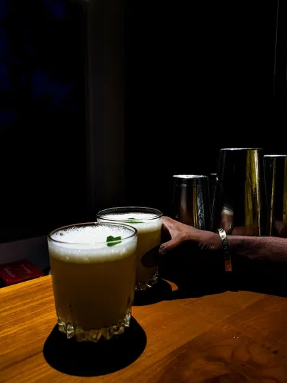 Two freshly made whiskey sours with a perfect foam top, ready to be served. The dramatic lighting highlights the texture and color of this classic cocktail.