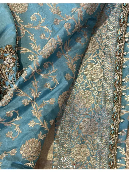 The rich texture of the teal blue Banarasi silk saree, perfectly complementing the heavily embroidered blouse. The combination of the woven pattern on the saree and the hand-embroidery on the blouse creates a look of unparalleled richness.