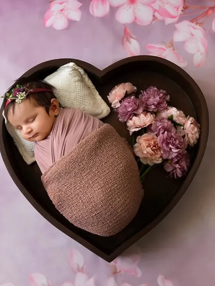 A newborn rests in a heart-shaped bowl against a dreamy floral background, an example of my artistic and styled newborn photography.