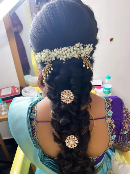 A close-up of a traditional South Indian bridal braid for Anusha's Varapooja. The hairstyle is decorated with pearl accessories and floral elements.