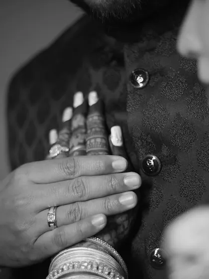 A close-up, black and white shot focusing on the couple's hands. The bride's hand rests on the groom's chest, a simple yet powerful gesture of connection and intimacy.