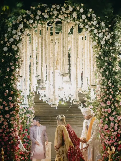 A stunning floral archway frames the couple during their wedding ceremony. The mandap is adorned with cascading white flowers, creating a dreamy, ethereal setting for their vows.