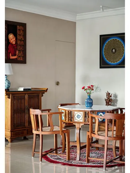 This cozy corner of the living area features a traditional Indian card table with inlaid tiles and chairs, set against a backdrop of unique art pieces collected by the family.