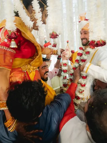 A fantastic candid shot from a fusion wedding ceremony. The bride is lifted on her family's shoulders during the varmala exchange, with everyone around sharing in the laughter and excitement.