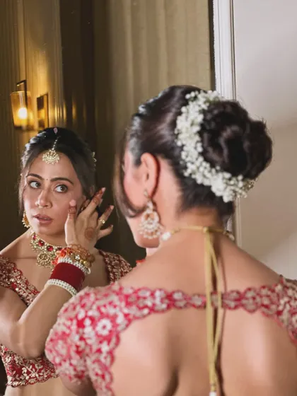 Simplicity, elegance, and grace. A beautiful shot of the bride looking in the mirror, with a classic red lehenga and a simple, elegant floral bun.