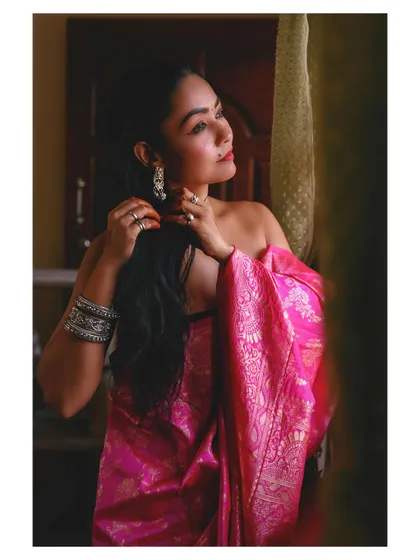 A candid and artistic portrait in a pink silk saree. The soft window light and the subject's pose create a sense of quiet reflection, highlighting the beauty of the moment.