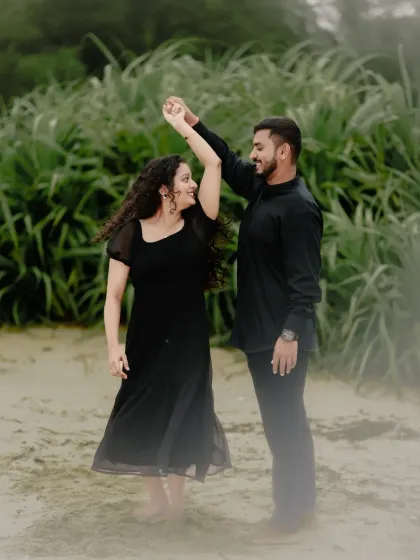 A couple in matching black outfits shares a dance on the beach, a simple and elegant pre-wedding shot.