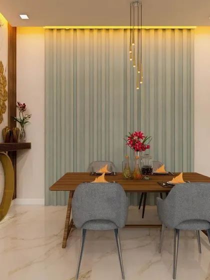 A contemporary dining setup featuring a simple wooden table and grey upholstered chairs. The space is defined by a large, ornate mirror and a cascading pendant light, adding a touch of glamour and sophistication.
