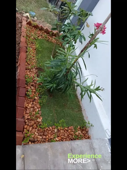 A small garden bed featuring a mix of grass, flowering plants, and a pebble border, all enclosed by a neat brick edge.