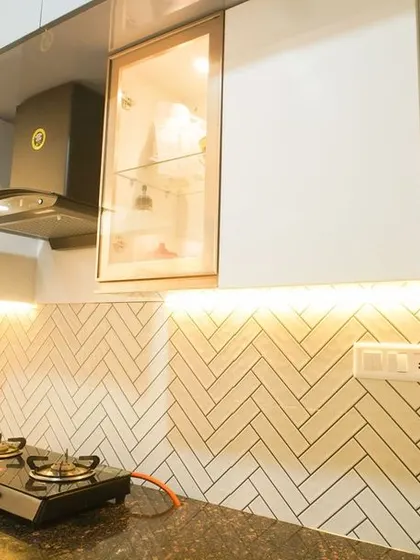 A close-up of a kitchen featuring a classic herringbone tile backsplash made of white subway tiles with dark grout. The under-cabinet lighting accentuates the pattern, creating a stylish and timeless look.