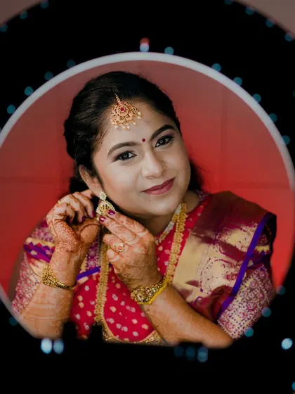 A creative shot of the bride getting ready. The ring light frames her face, highlighting the perfectly blended makeup and the traditional maang tikka, essential parts of the South Indian bridal look.