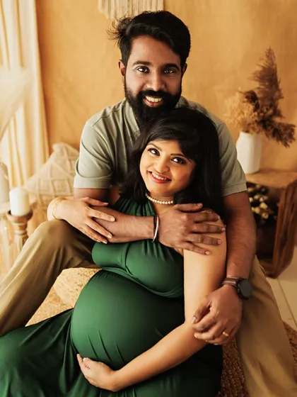 A cozy and intimate portrait of an expecting couple in a boho setting. The rich green dress and earthy tones create a warm and inviting atmosphere.