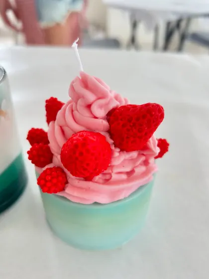 A close-up of a beautifully detailed cupcake candle with raspberry and heart toppings.