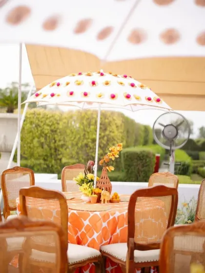 Guest tables at the Haldi are set with patterned orange tablecloths and shaded by custom-printed umbrellas, creating a cohesive and festive look.