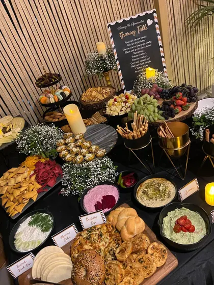 A stunning grazing table I set up for a 70th birthday party. The spread includes a variety of cheeses, dips, breads, and fruits, all beautifully styled with baby's breath and candles.